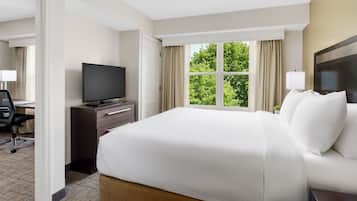 A hotel room with a large bed, a TV on a dresser, a desk with a chair, and a window with curtains.