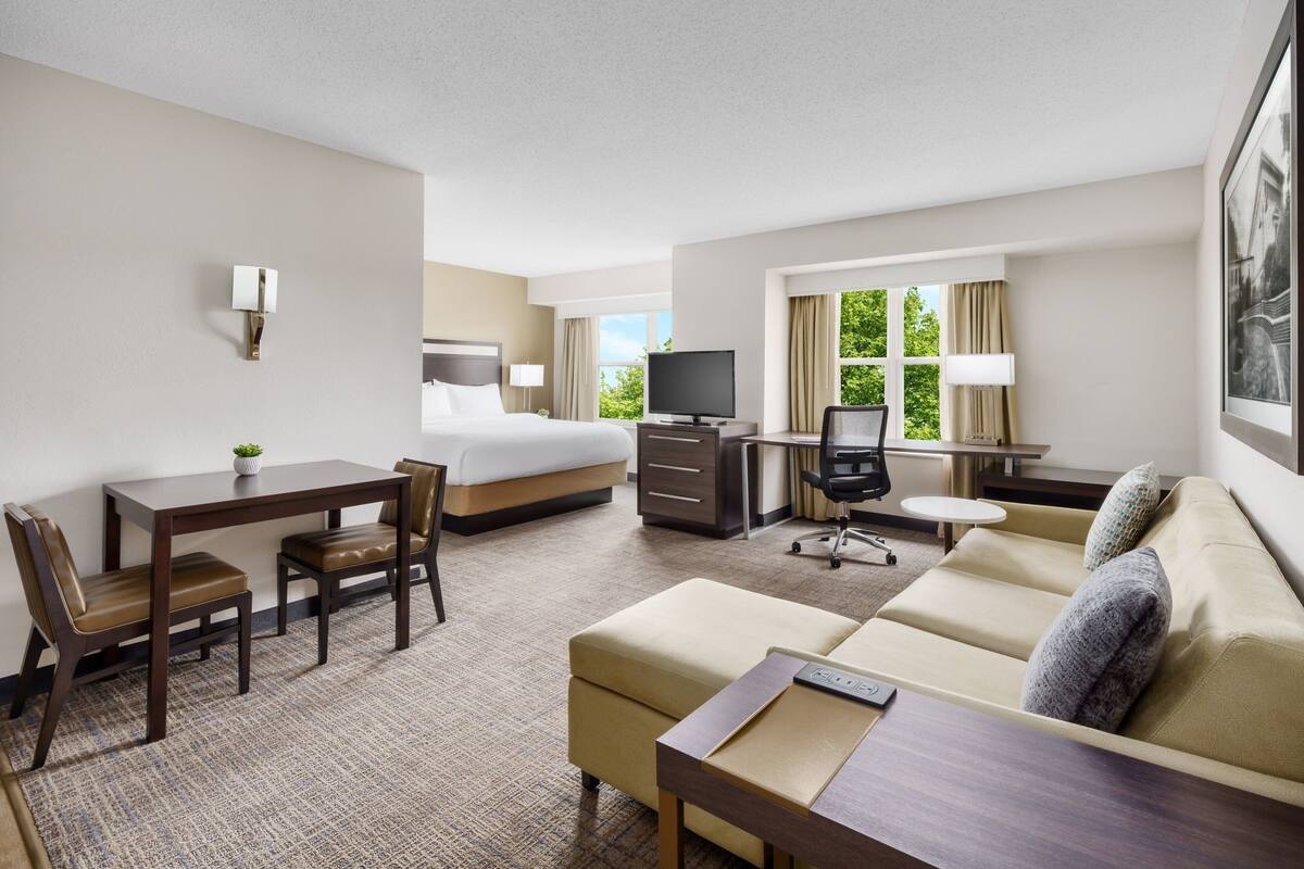Ein Hotelzimmer mit Bett, Schreibtisch, Sofa und Fernseher.