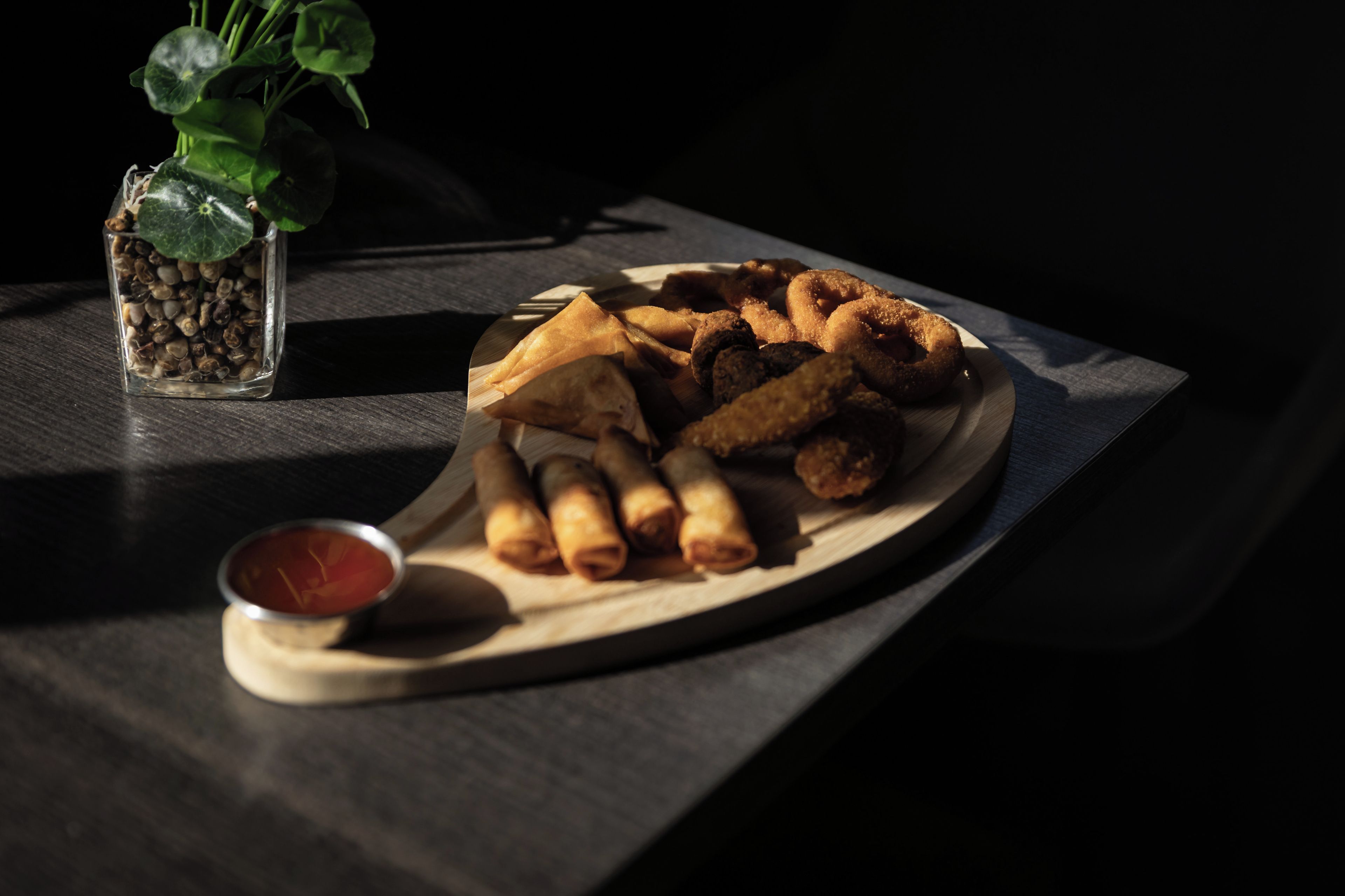 Un plato de aperitivos fritos y un cuenco pequeño con salsa sobre una tabla de madera.