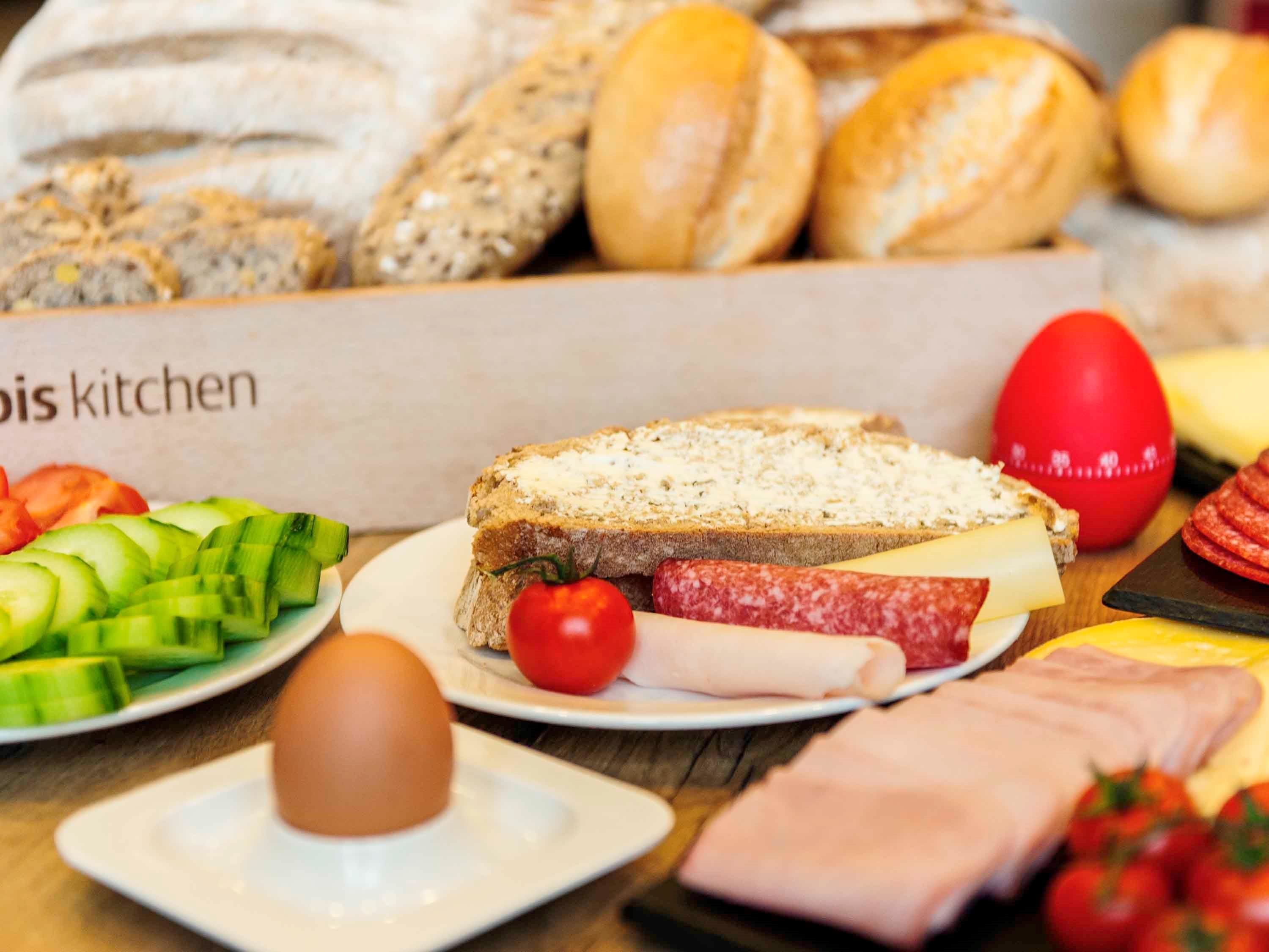 Een ontbijt met brood, kaas, ham en groenten op een houten tafel.