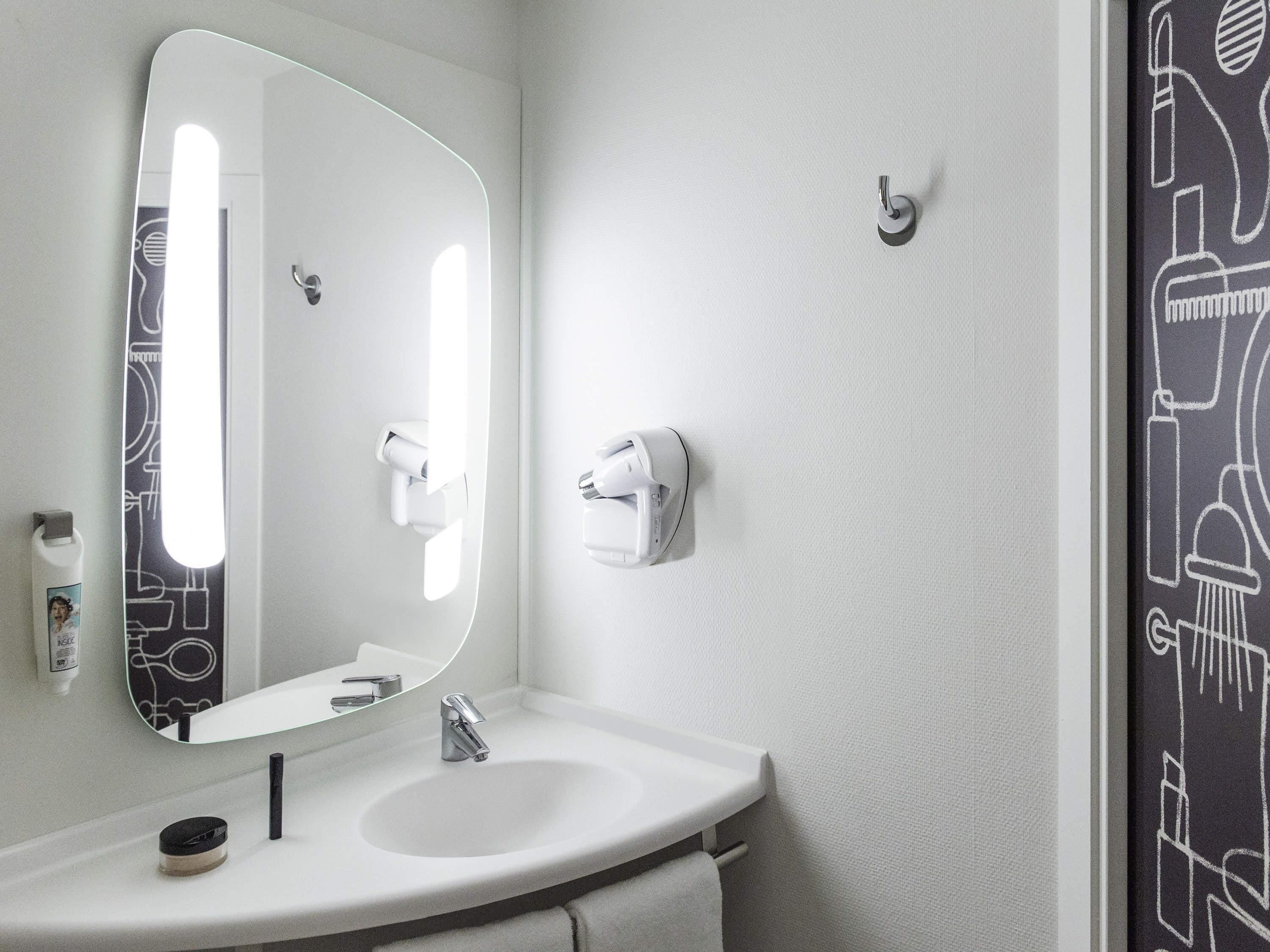 Un baño con un lavabo blanco, un espejo, un perchero para toallas y un secador de pelo montado en la pared.