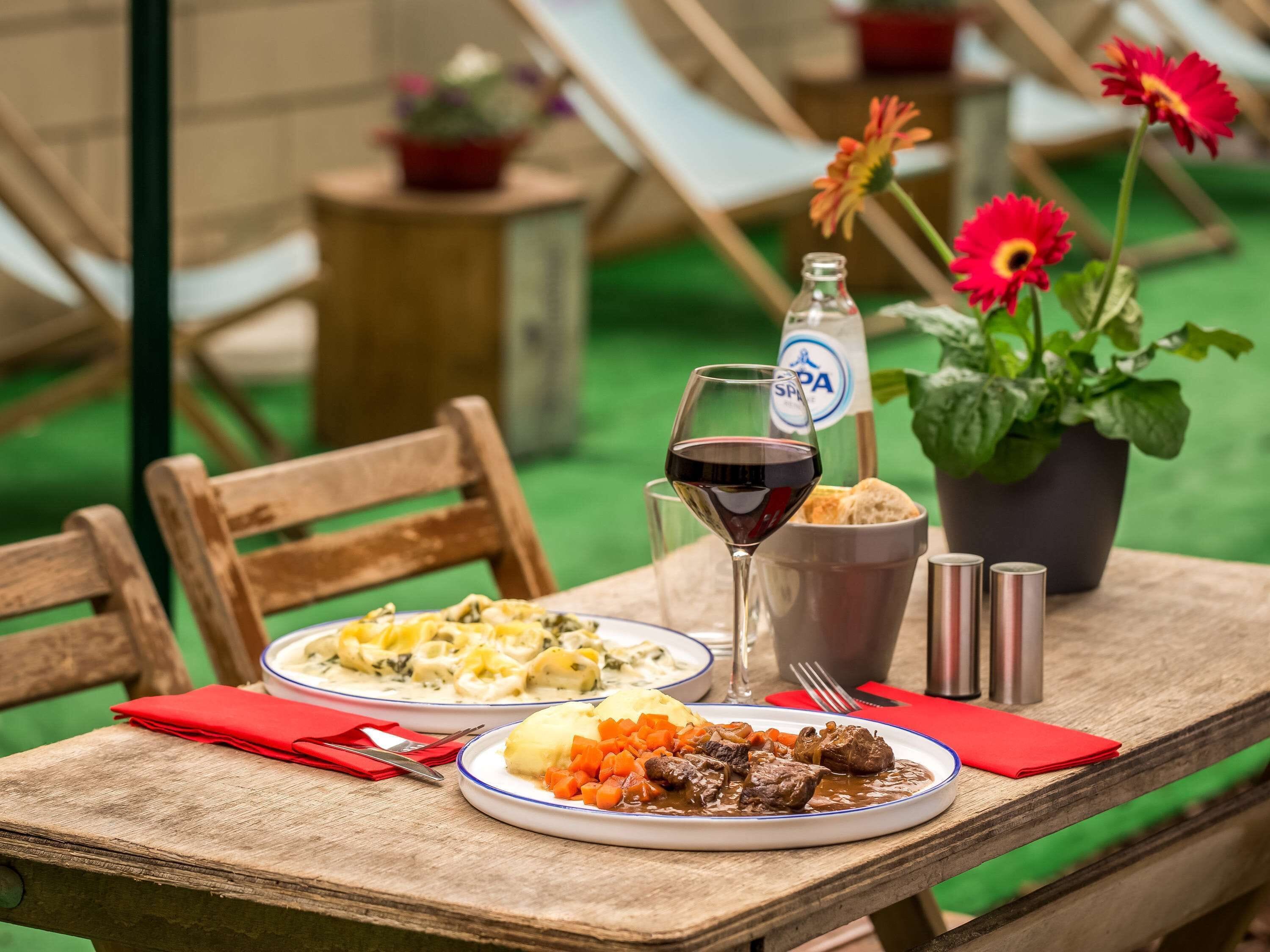 A wooden table with plates of food, a glass of red wine, and a bottle of water.