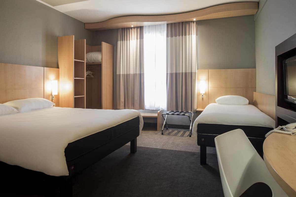 Habitación de hotel con dos camas, un escritorio, una silla, un televisor y un armario.