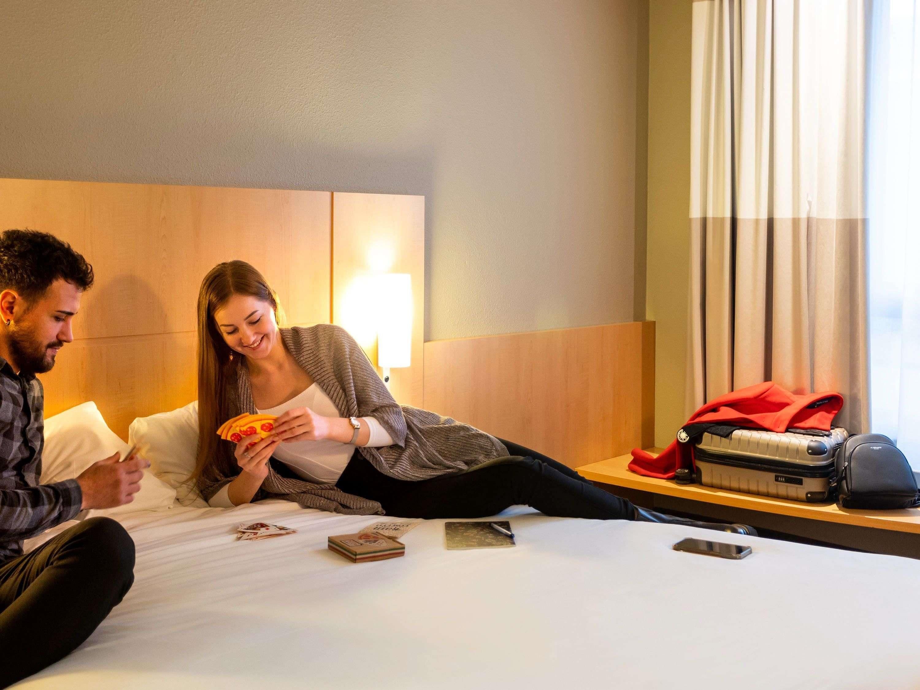 A hotel room with a bed, a nightstand with a lamp, and a window with curtains.