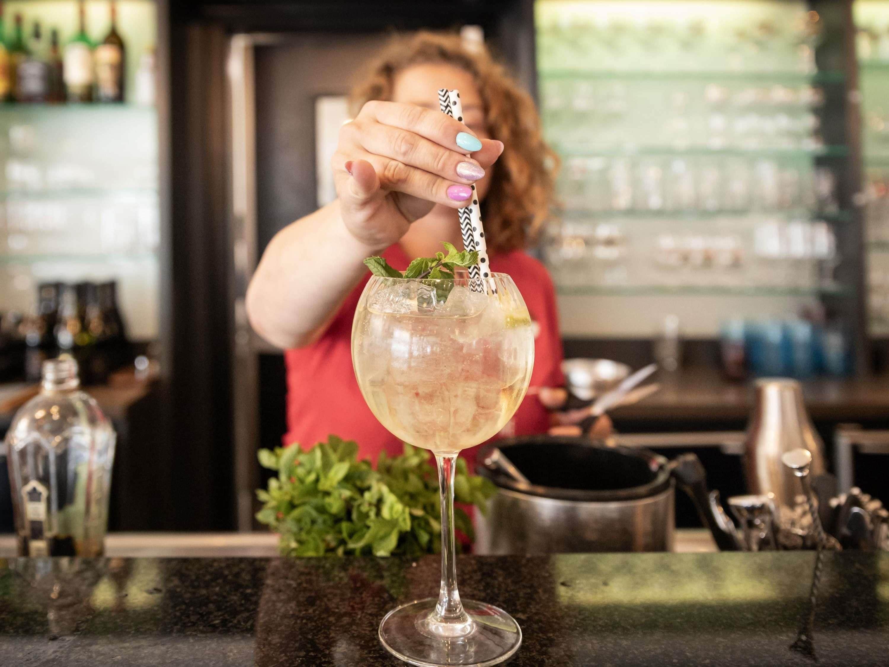 Een bartender bereidt een cocktail met een decoratief rietje in een glas.