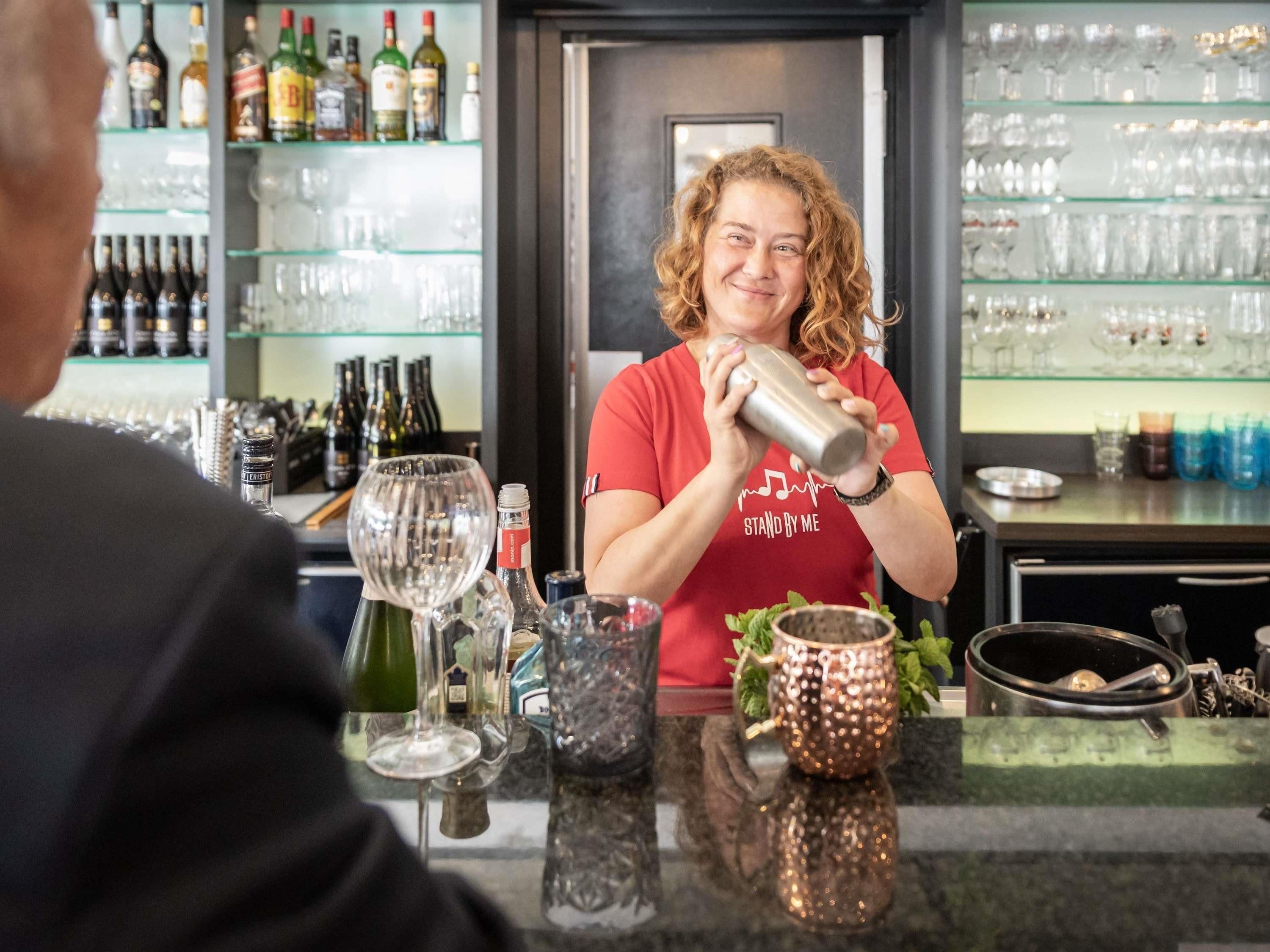 A bartender preparing a drink behind a bar with various bottles and glasses.