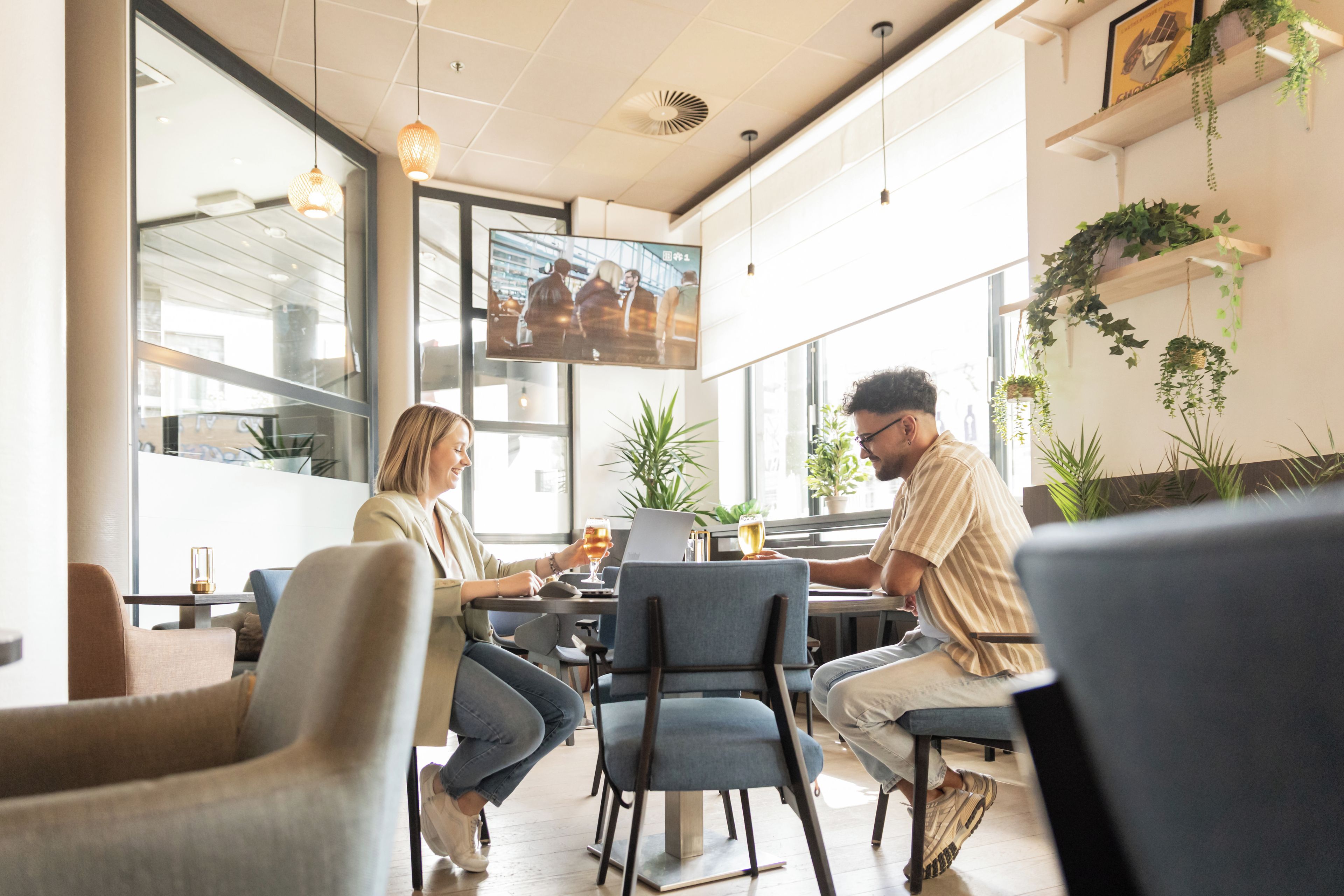 Un café moderne avec de grandes fenêtres, des sièges confortables et des plantes d’intérieur.