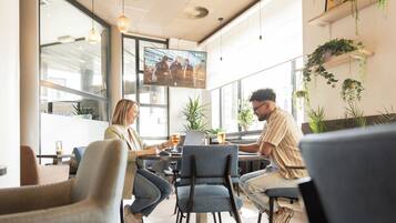 Una cafetería moderna con amplios ventanales, asientos cómodos y plantas de interior.