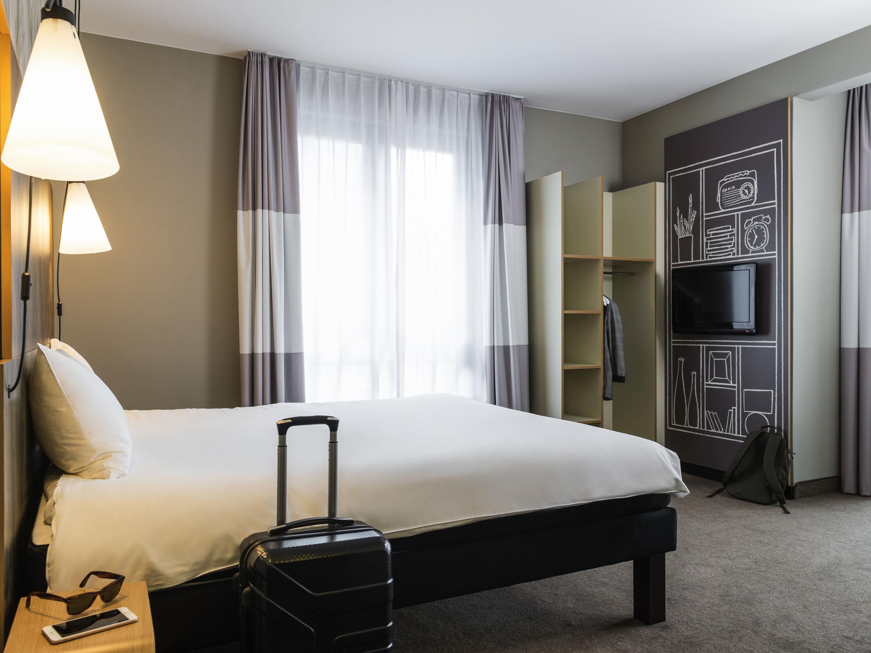 Una habitación de hotel con cama, maleta, televisión y armario.