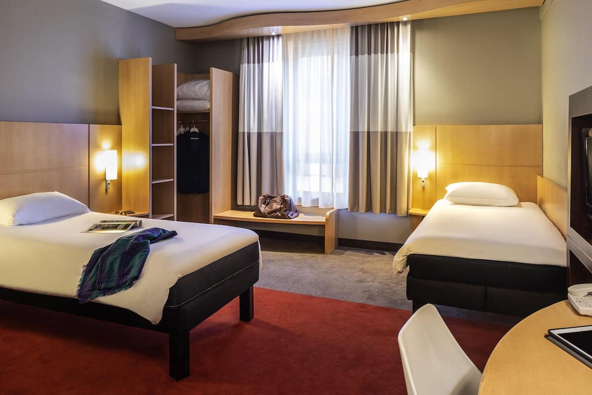 Habitación de hotel con dos camas, un escritorio, una silla, un televisor y un armario.