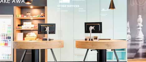 A reception area with two reception desks, a refrigerator stocked with beverages, and a wall displaying room rates and services.