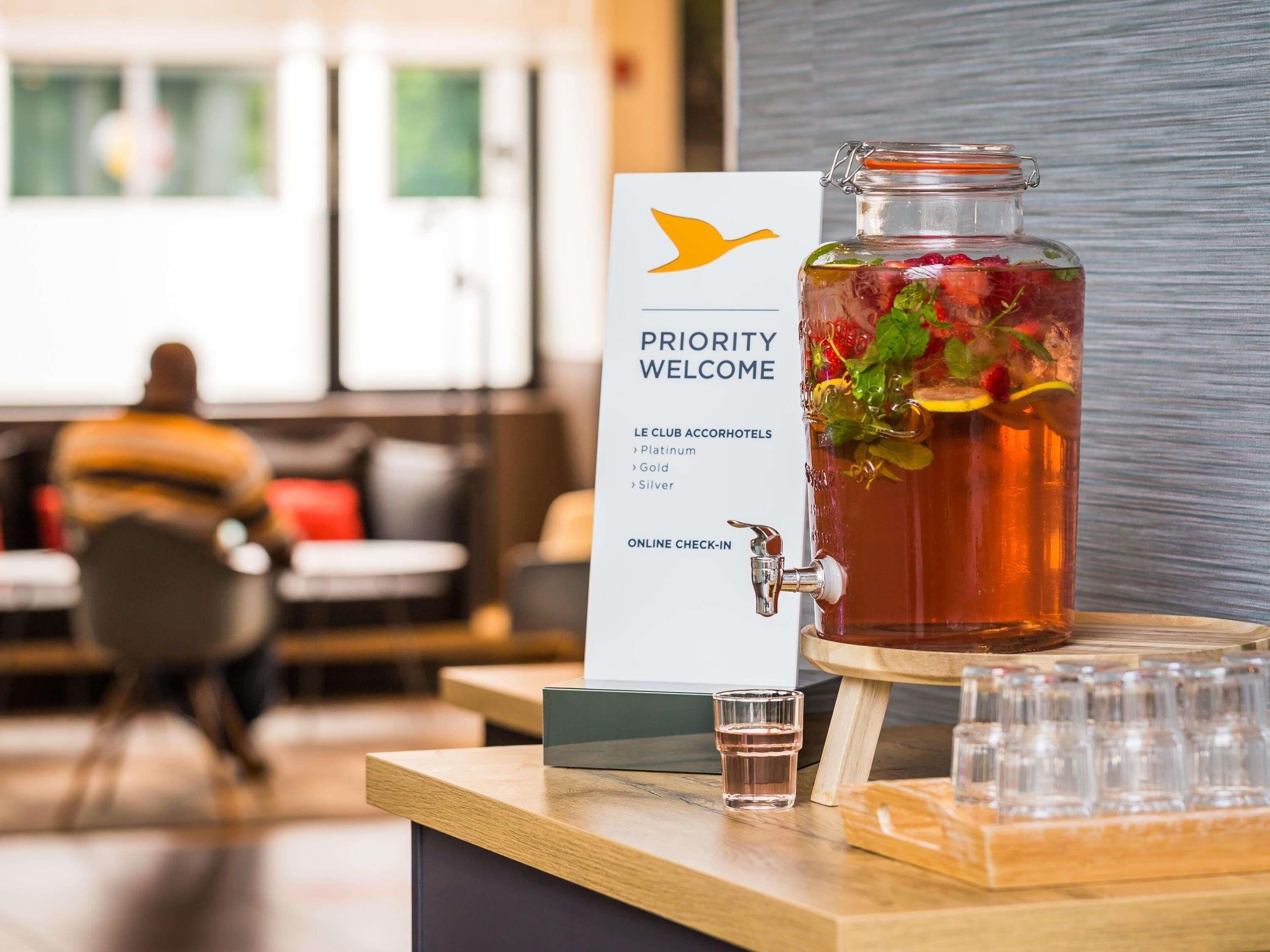 A priority welcome sign with a glass jar of iced tea, a shot glass, and a sign for online check-in at the LE CLUB ACCORHOTELS.