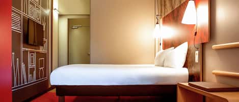 A hotel room with a bed, a TV, a red carpet, and a wall with a geometric design.