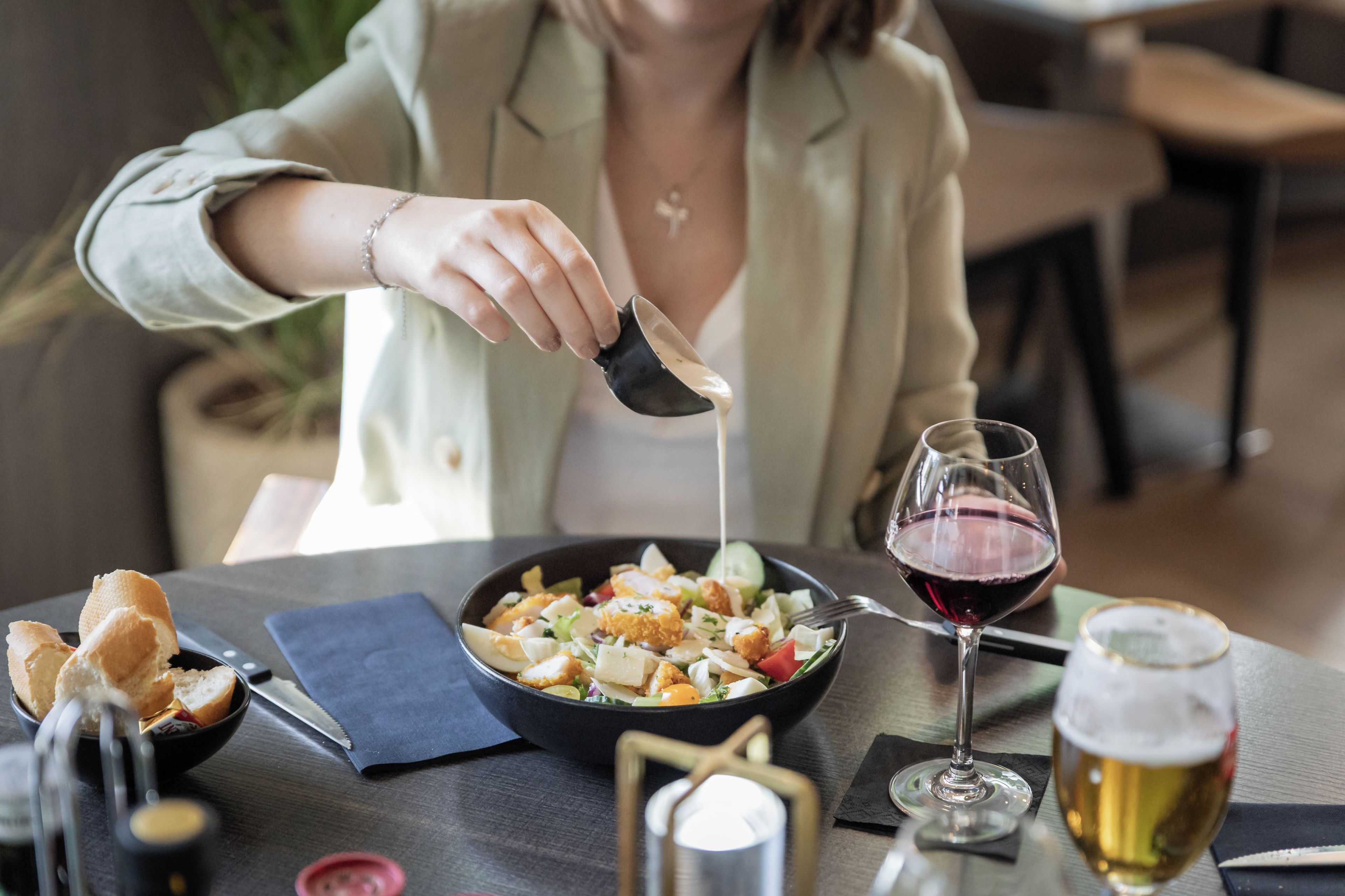 Eine Person isst an einem Tisch mit einer Schüssel Essen, einem Glas Rotwein und einem Glas Bier.