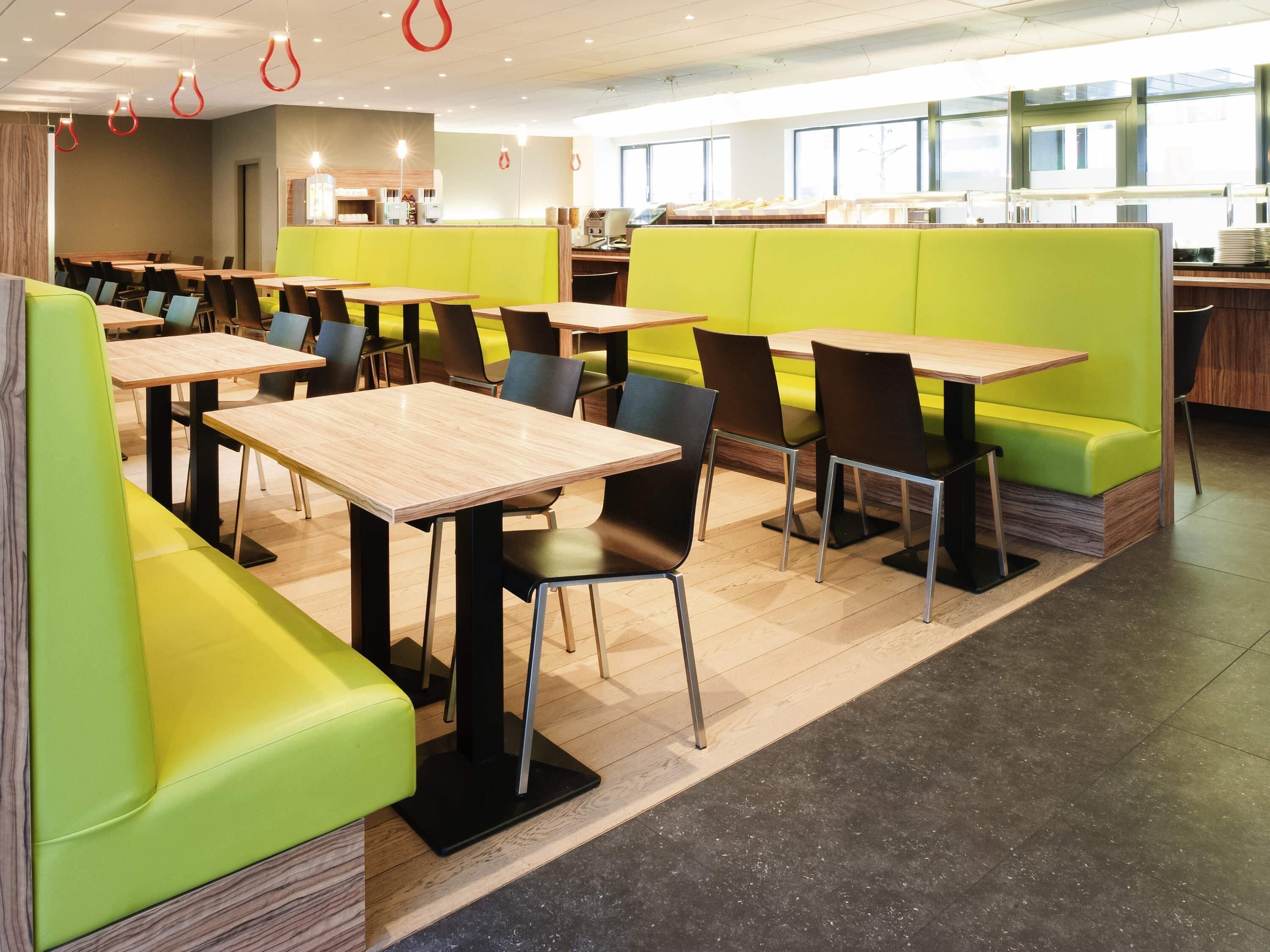 Un espace repas moderne, doté de plusieurs tables et chaises, de sièges d’un vert vif et d’un environnement propre et bien éclairé.