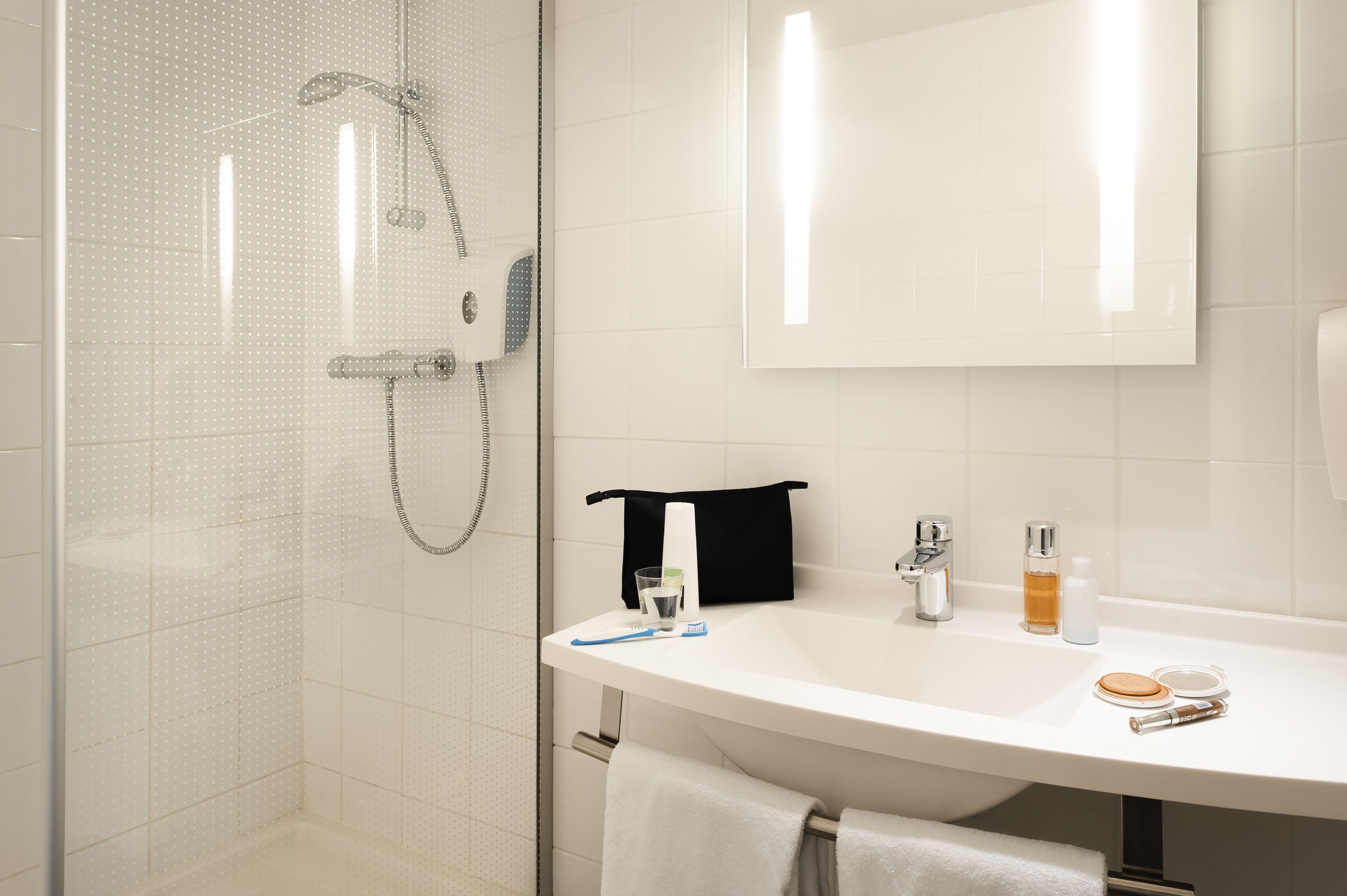 A modern bathroom with a glass shower enclosure, a white sink with toiletries, and a mirror above the sink.