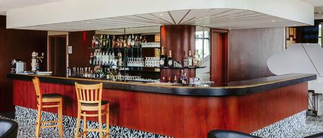 A bar area with a curved counter, wooden chairs, and a patterned carpet.
