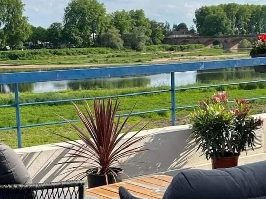 Una terraza con dos sillas de mimbre, una mesita y vistas a un río y zonas verdes.