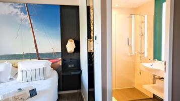 Habitación de hotel con cama, un pequeño espacio de descanso, vista al mar y baño con lavabo y espejo.
