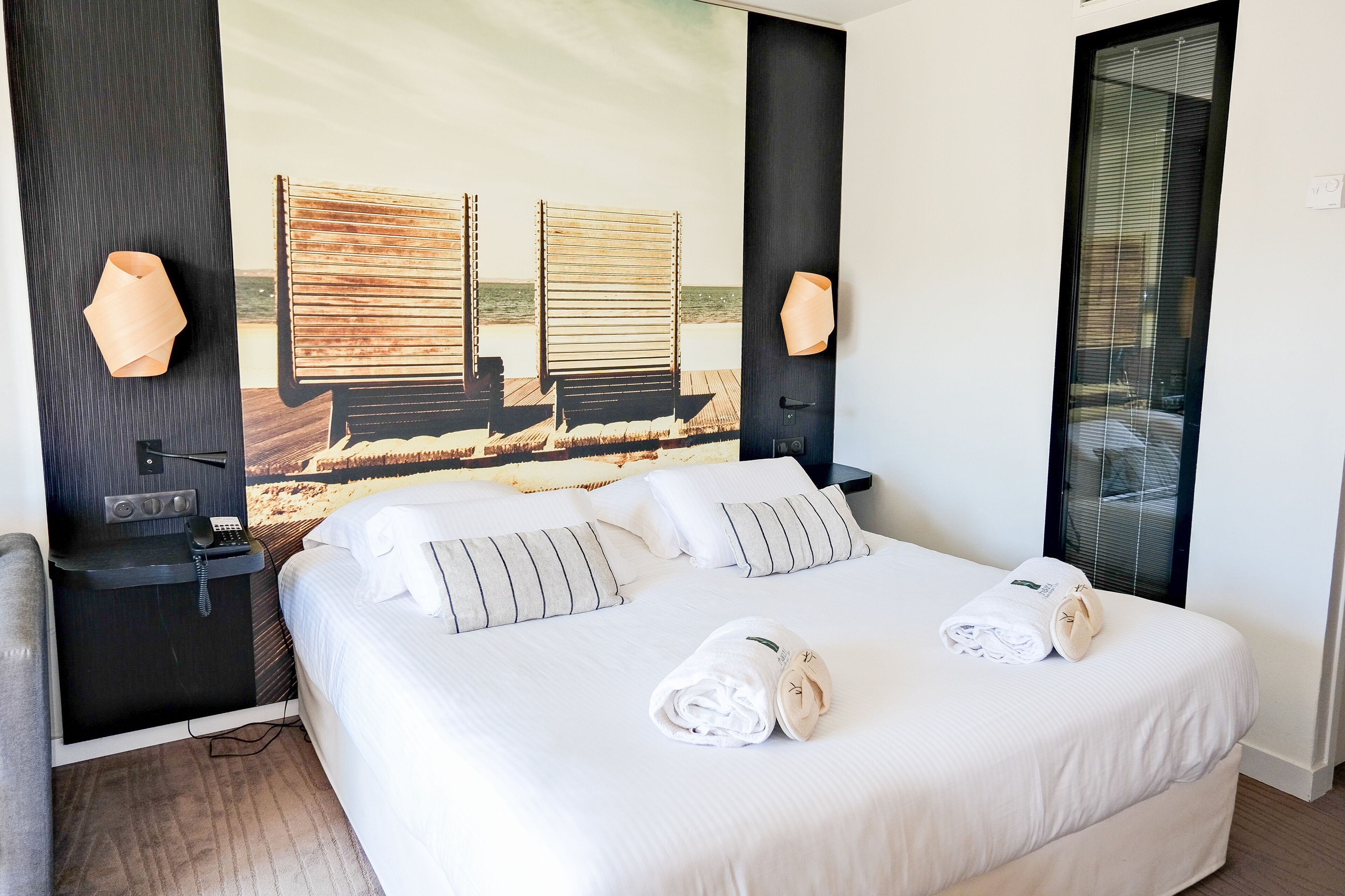 A hotel room with a large bed, two bedside tables, a desk with a phone, and a beach-themed wall mural.