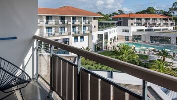 A balcony with a view of a hotel building, a swimming pool, and palm trees.