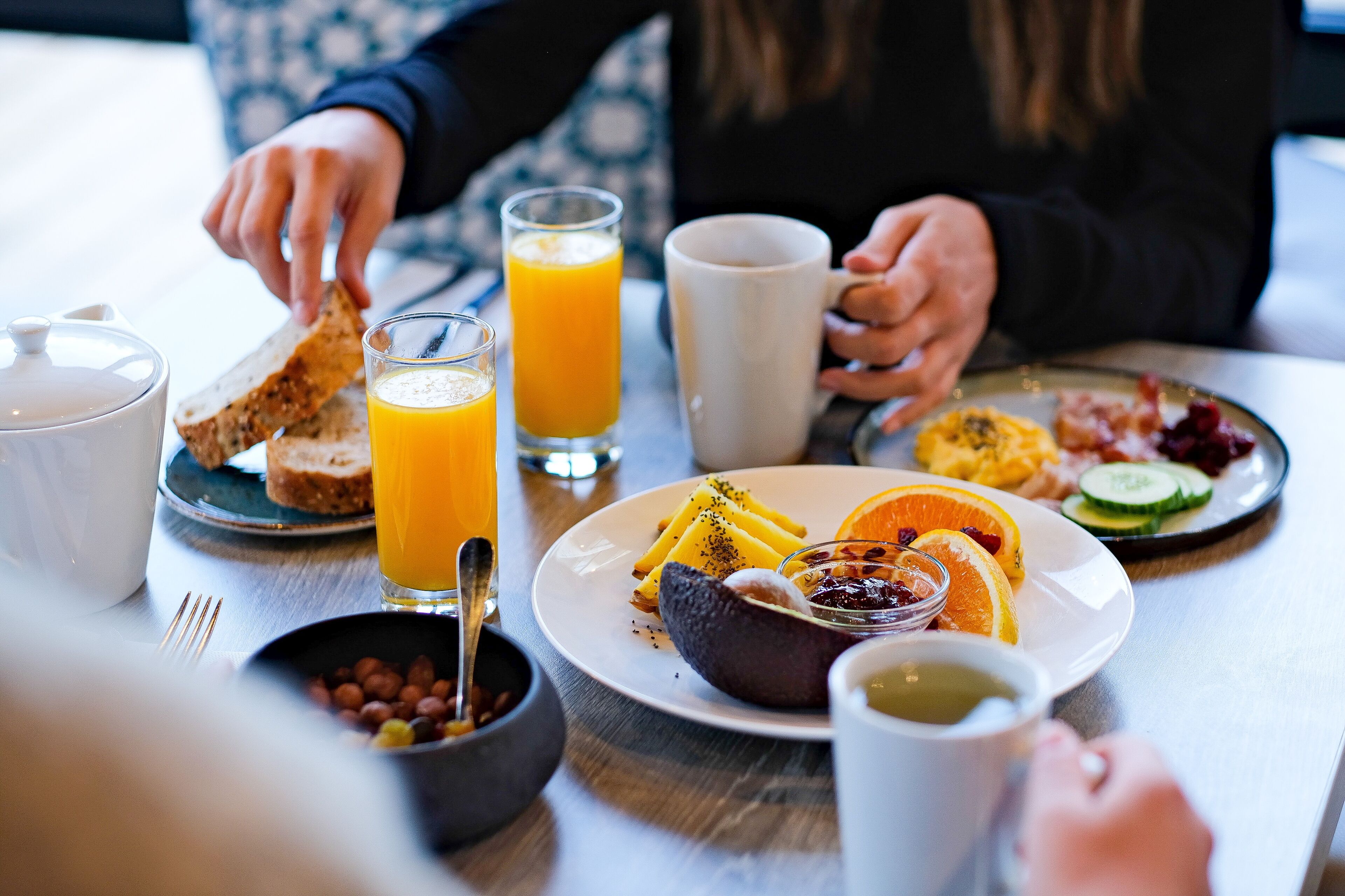 Desayuno con tostadas, jugo de naranja, frutas variadas y huevos en un plato.