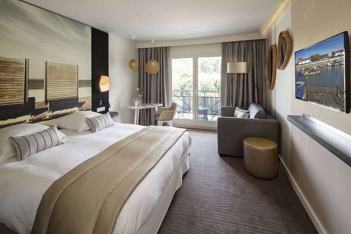 Ein Hotelzimmer mit einem großen Bett, einer Sitzecke mit Tisch und einem Balkon mit Blick auf das Wasser.