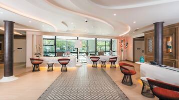 Eine großzügige Lobby mit modernem Design, ausgestattet mit einer Rezeption, einer Sitzecke mit Stühlen und großen Fenstern mit Blick ins Freie.