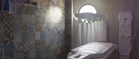 A modern bathroom with a mosaic tile wall, a standing shower, and a white examination table.