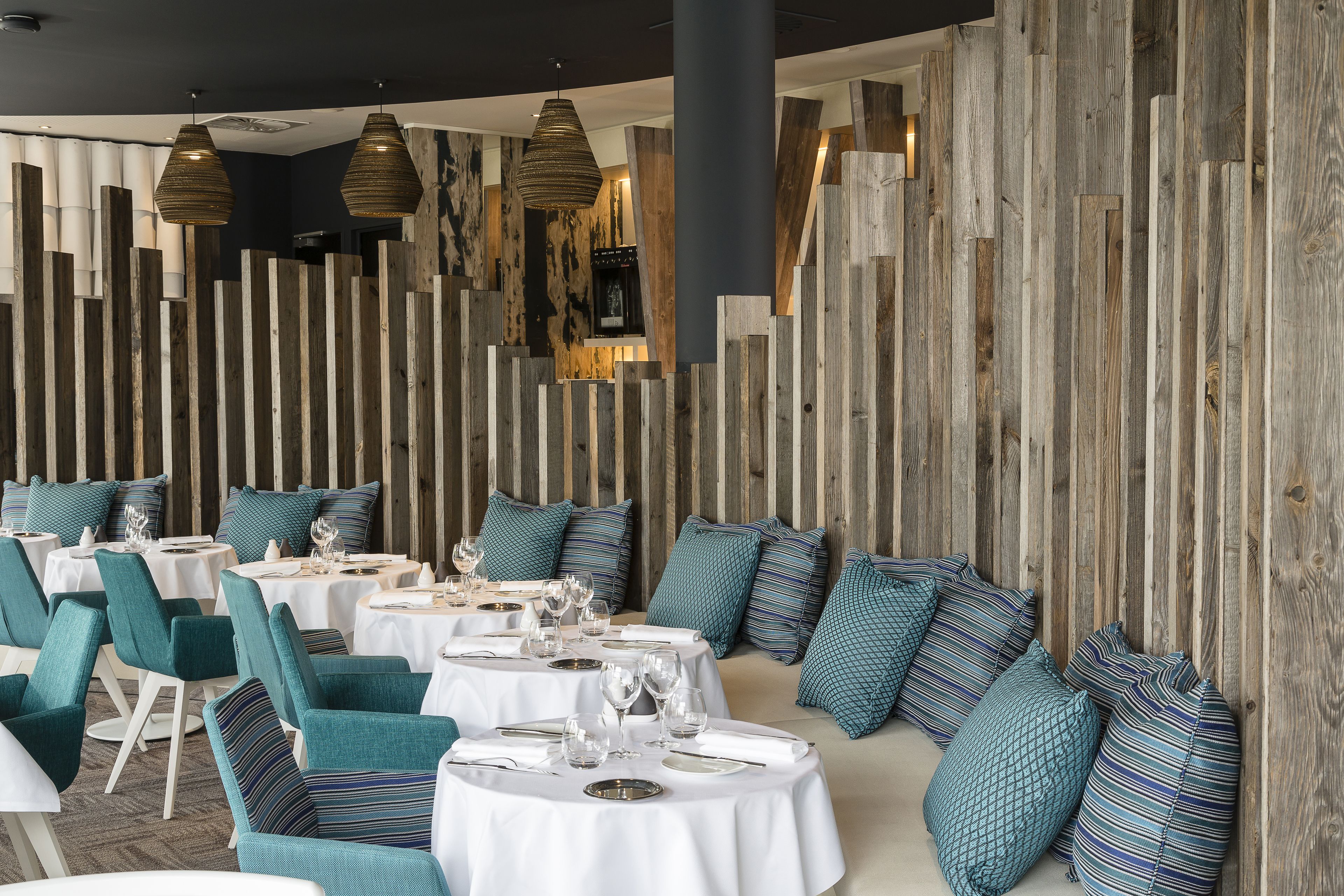 A restaurant with round tables, teal chairs, and wooden panel walls.