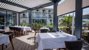 Enjoy al fresco dining on the covered patio with tables set amidst a beautiful landscape and building views.