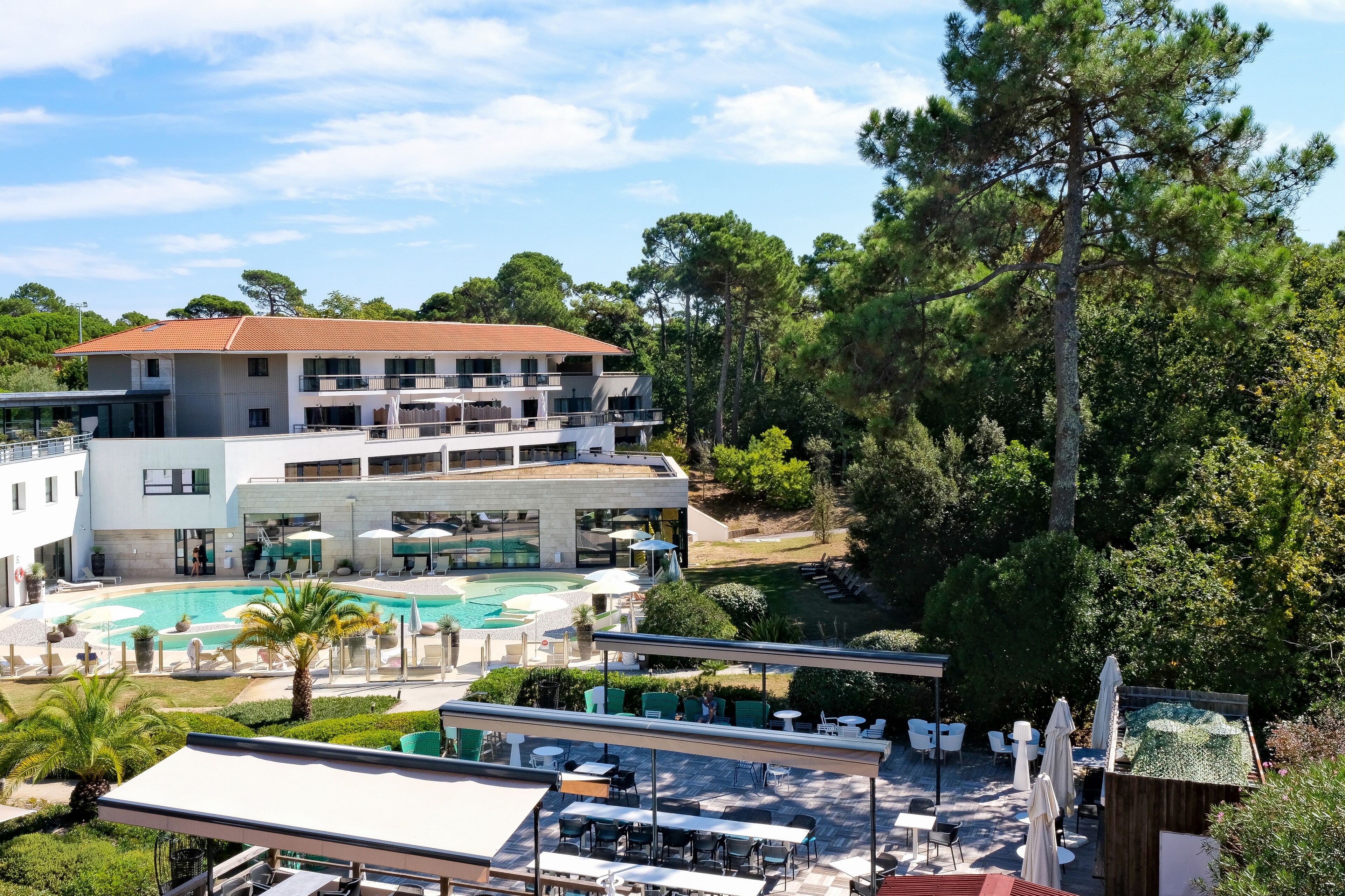 A modern hotel with a rooftop pool, outdoor seating, and lush greenery.