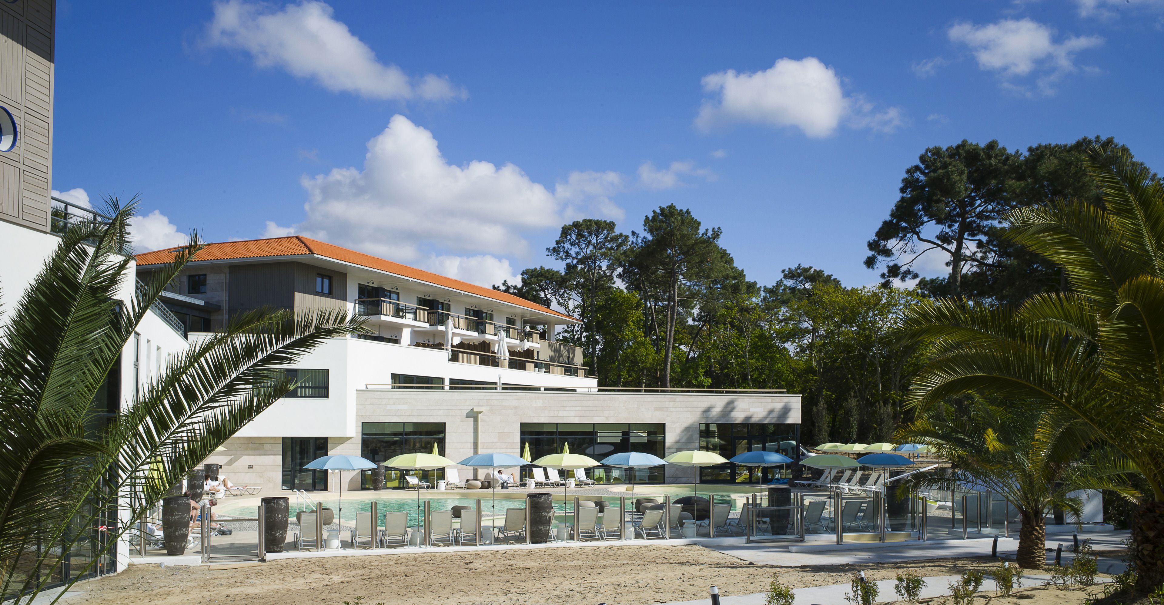 Un hotel moderno con zona de piscina, varios niveles y mobiliario exterior con sombrillas.