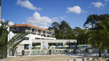 Un hotel moderno con zona de piscina, varios niveles y mobiliario exterior con sombrillas.