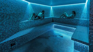 A blue-tiled indoor pool with two people relaxing on the steps. - Hôtel & Spa - Thalazur Arcachon (Arcachon)