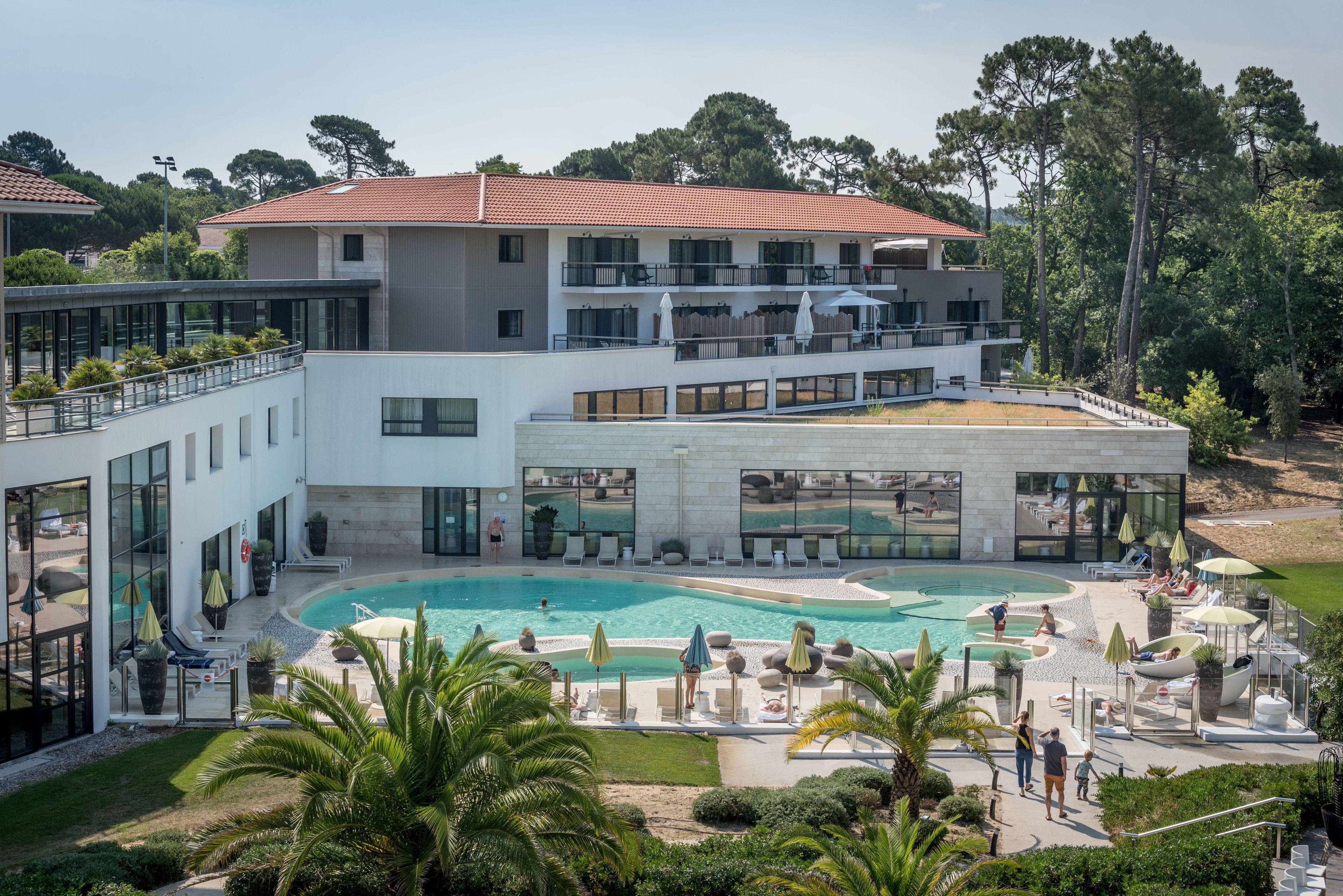 A multi-story hotel with a swimming pool, outdoor seating, and lush landscaping.