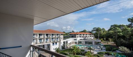 A balcony with a view of a hotel courtyard, including a pool and outdoor seating.