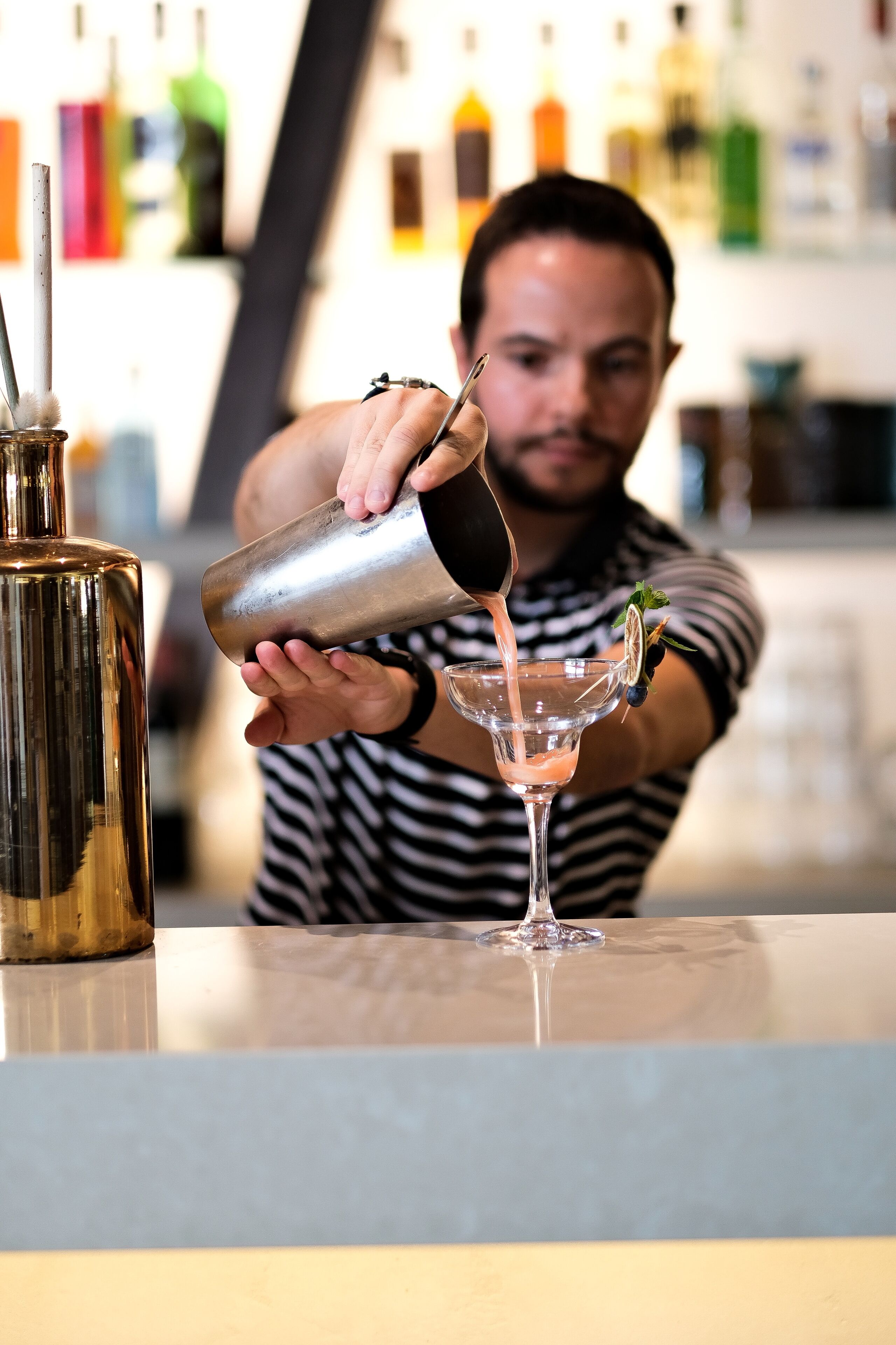 A bartender pouring a drink into a martini glass.