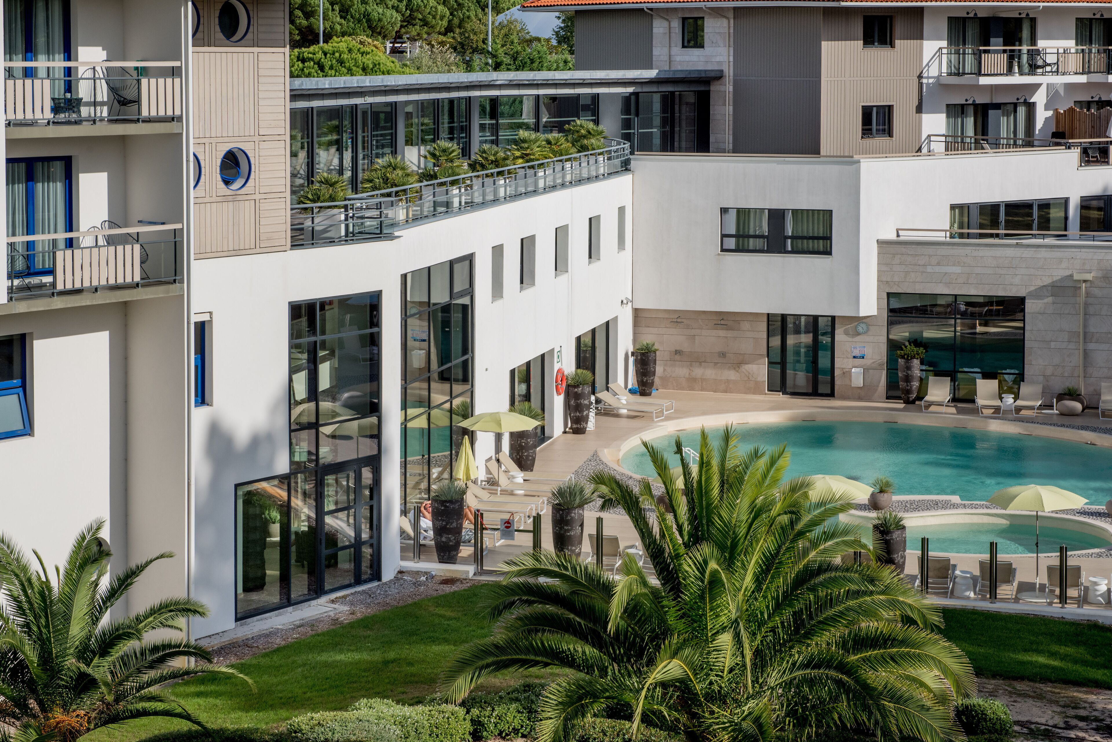 A modern hotel with a rooftop pool, outdoor seating, and lush landscaping.