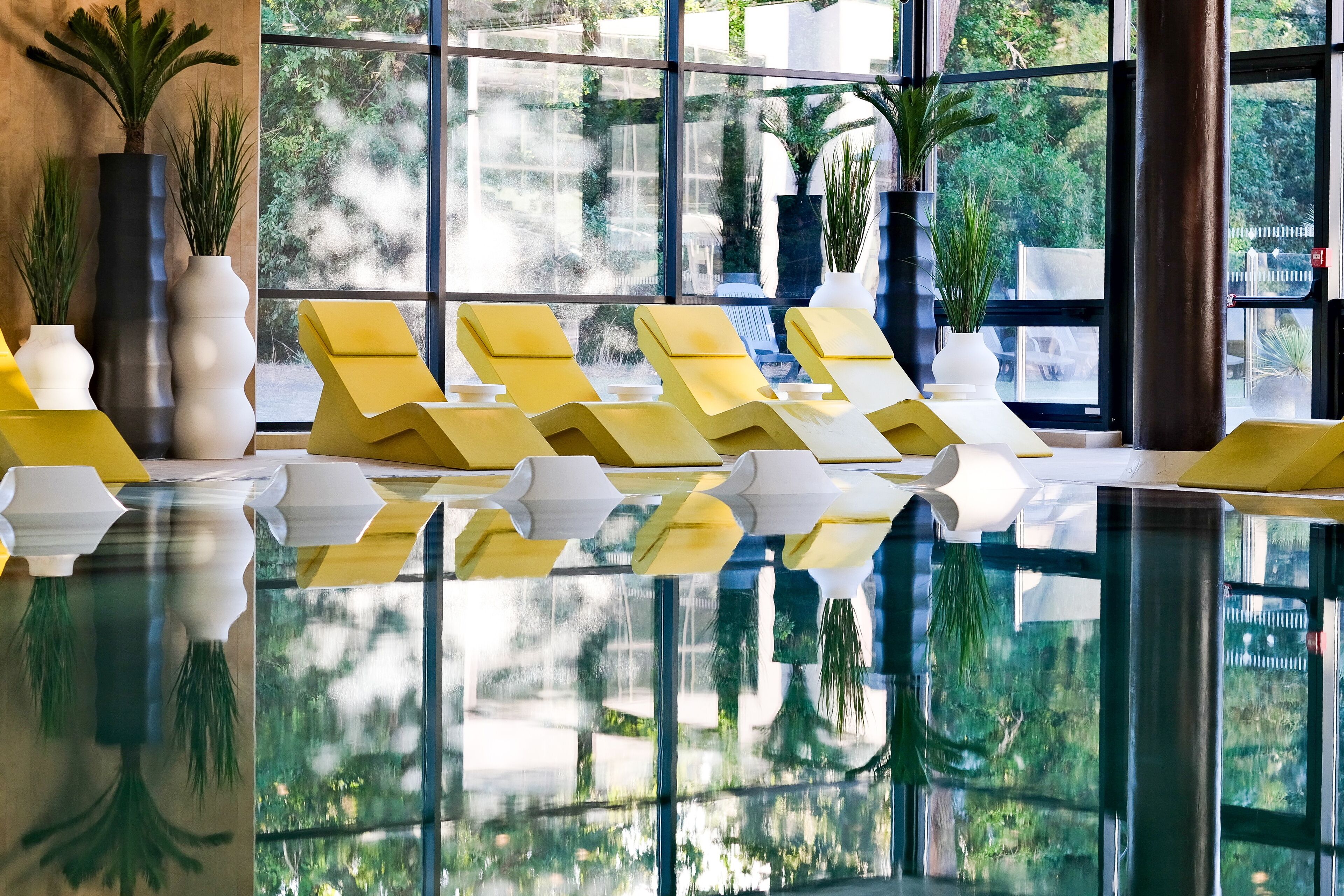 A pool area with yellow lounge chairs and potted plants.