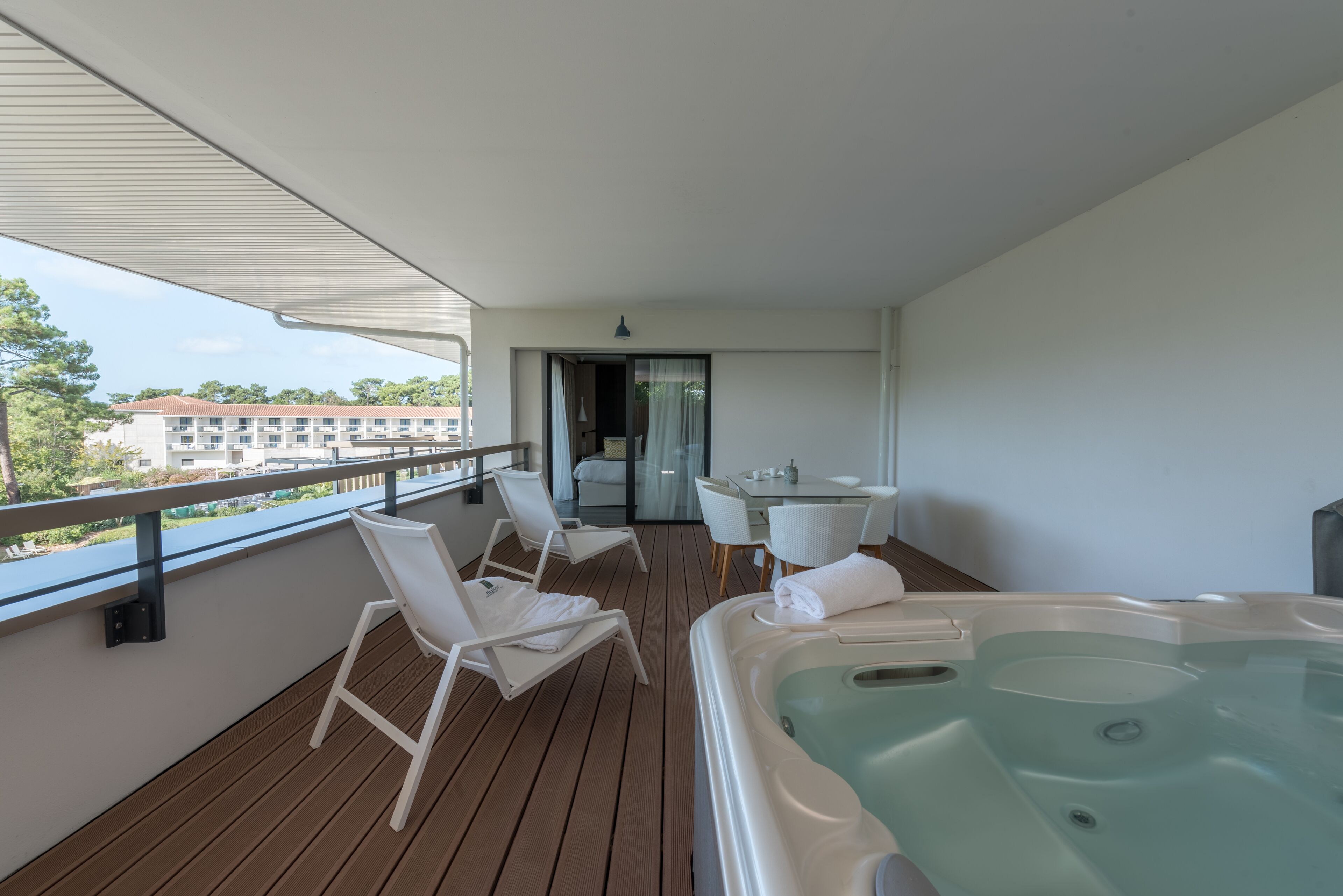 Un balcón con piso de madera, sillones blancos, un jacuzzi y una mesa con sillas.