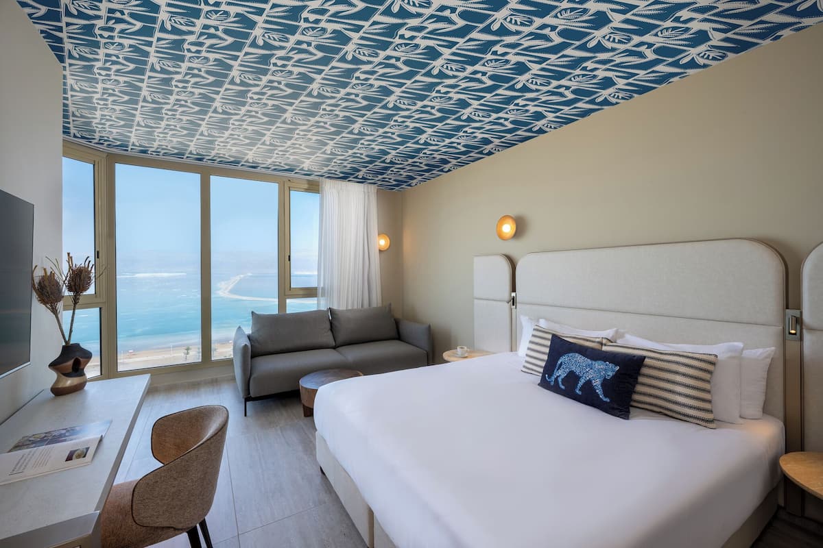 A hotel room with a large bed, a sofa, a desk, and a view of the sea.