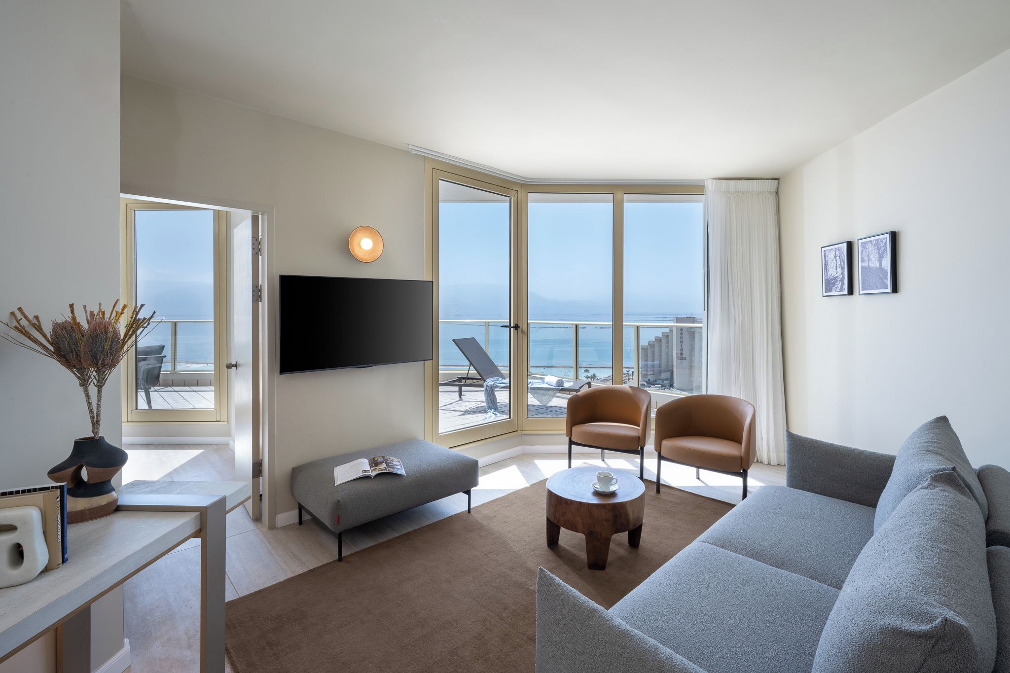 Una sala de estar moderna con un ventanal grande, un televisor de pantalla plana, un sofá gris, dos sillones y una mesa de centro.