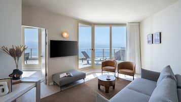 Una sala de estar moderna con un ventanal grande, un televisor de pantalla plana, un sofá gris, dos sillones y una mesa de centro.