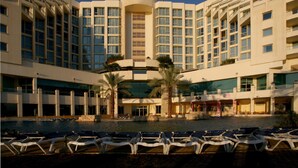 A hotel with a central courtyard, multiple balconies, and a pool area with lounge chairs. - Leonardo Plaza Dead Sea (Tamar)