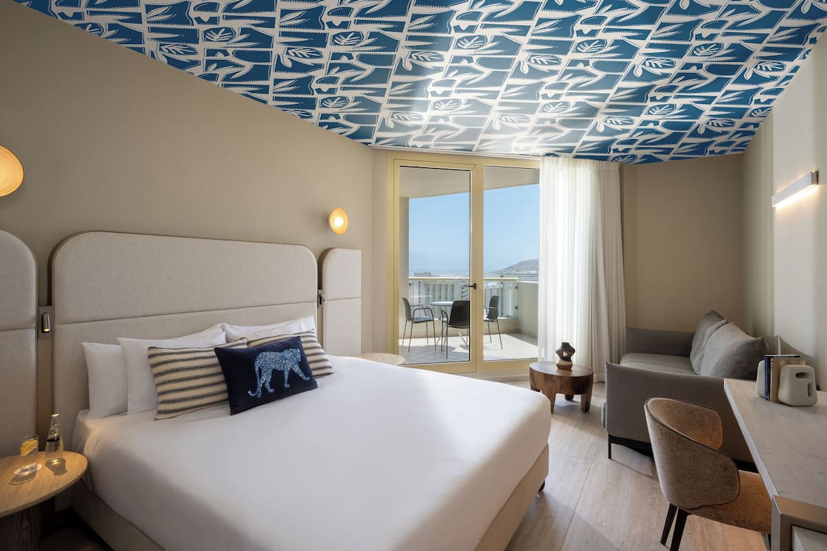 A hotel room with a bed, a sofa, a dining table, and a view through a glass door.