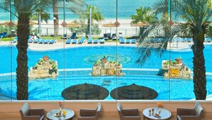 A poolside area with lounge chairs, a dining table with chairs, and a view of the ocean. - Leonardo Plaza Dead Sea (Tamar)