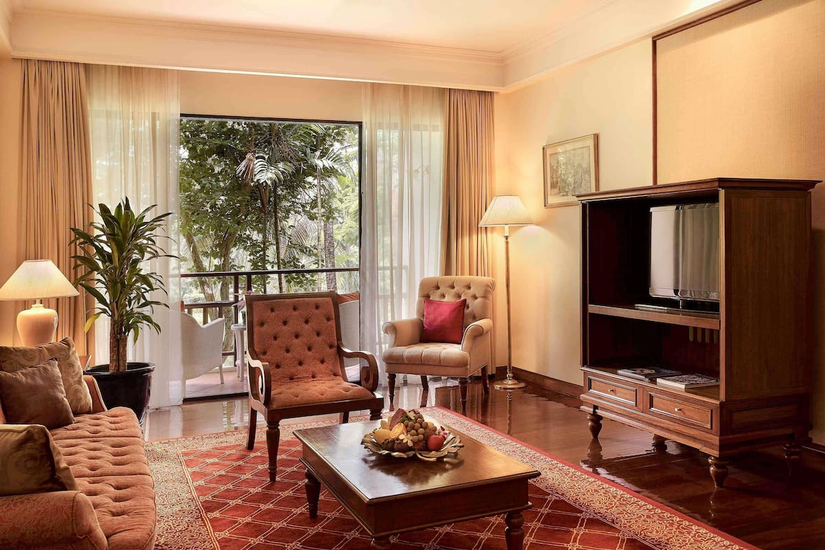 A well-furnished living room with a sofa, two armchairs, a coffee table, a television, and a potted plant.
