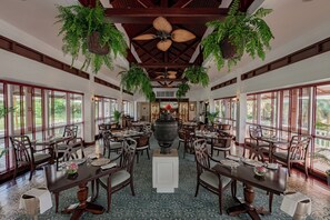 A spacious dining area with multiple tables and chairs, large windows, and hanging plants. - Sofitel Angkor Phokeethra Golf & Spa Resort (Siem Reap)