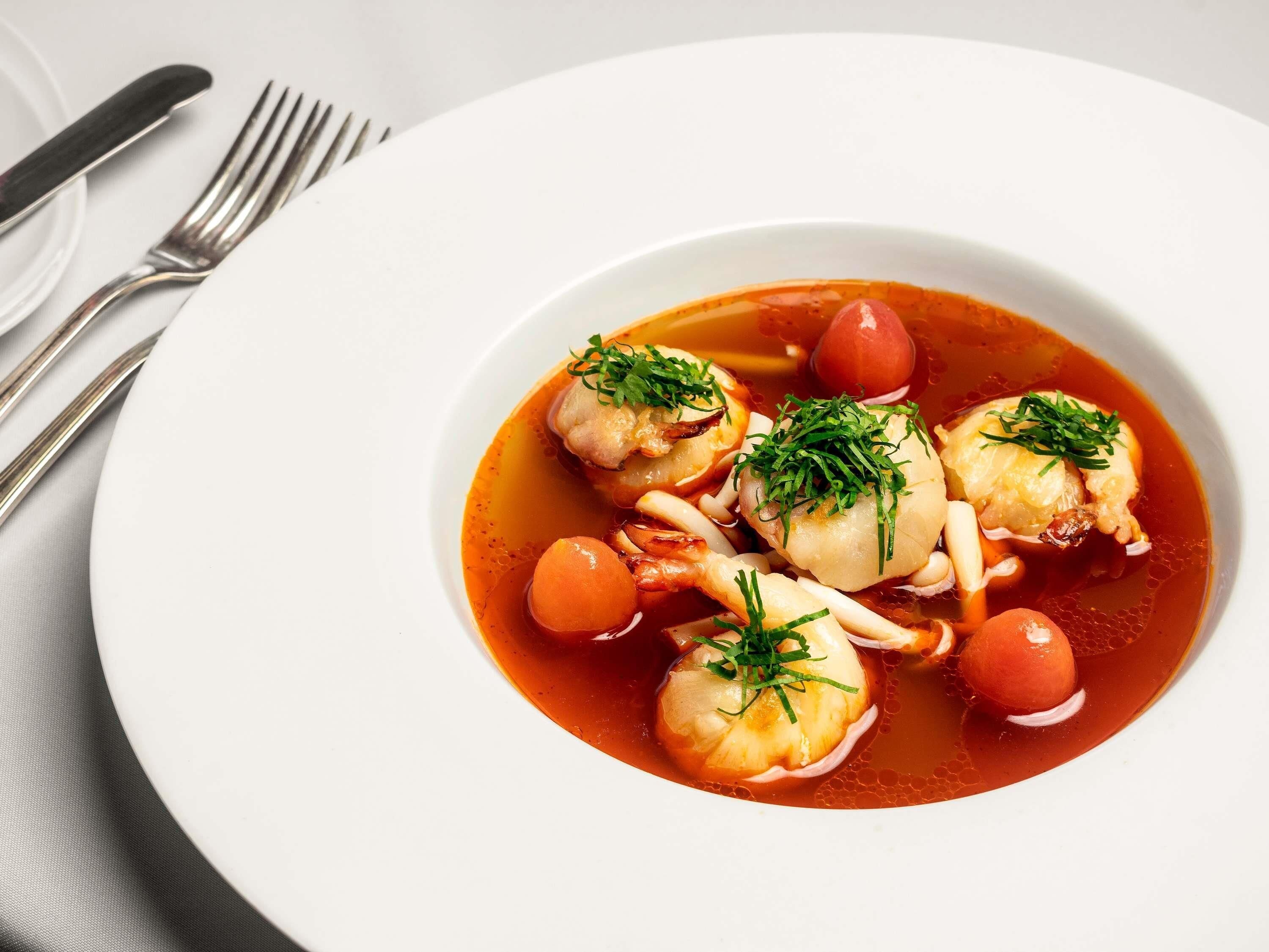 Un plato blanco con un guiso de mariscos, que incluye mejillones y camarones, adornado con hierbas.
